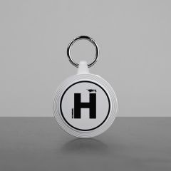 Geschlossener runder Behälter in Weiß mit schwarzer Aufschrift: Helipad, Minidrohne und SCHIEBEL, dazu ein Schlüsselring